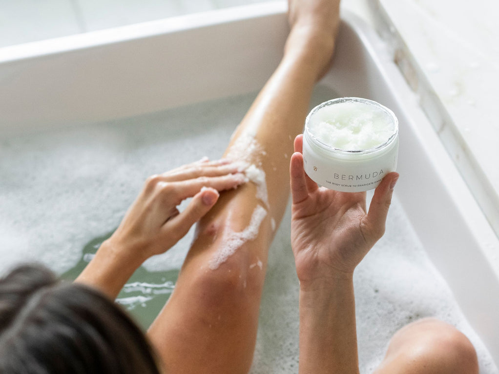 A woman in a bath holding a jar of Bushbalm scrub